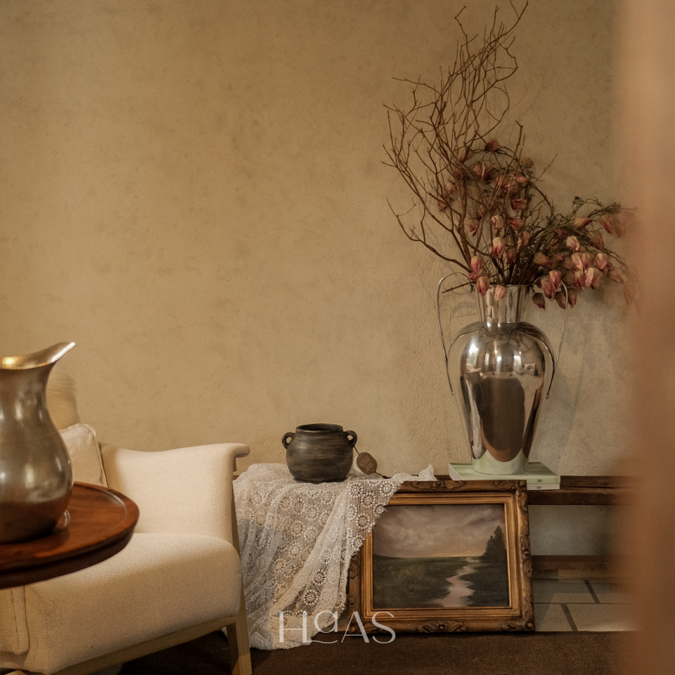 WANGSA chrome vase styled on a stand beside a cream armchair in a living room