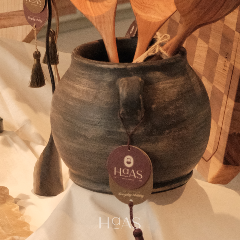 Close-up of the TANO clay vessel's rounded body and handle, holding dried stems