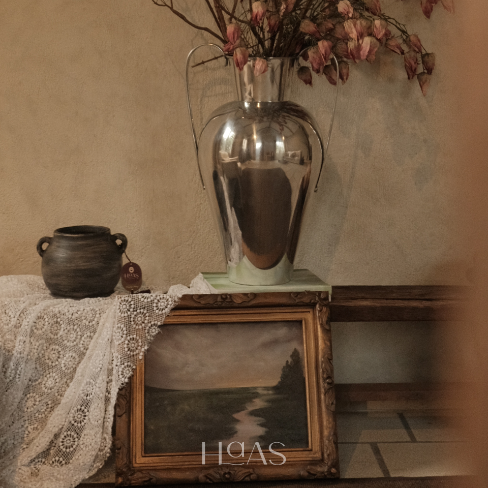 TANO clay vessel on a console behind a tall shiny vase and a framed landscape painting