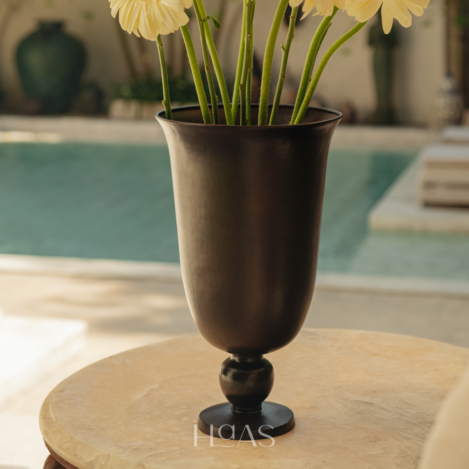 PILAR brass vessel holding pale blooms on a round table beside a pool